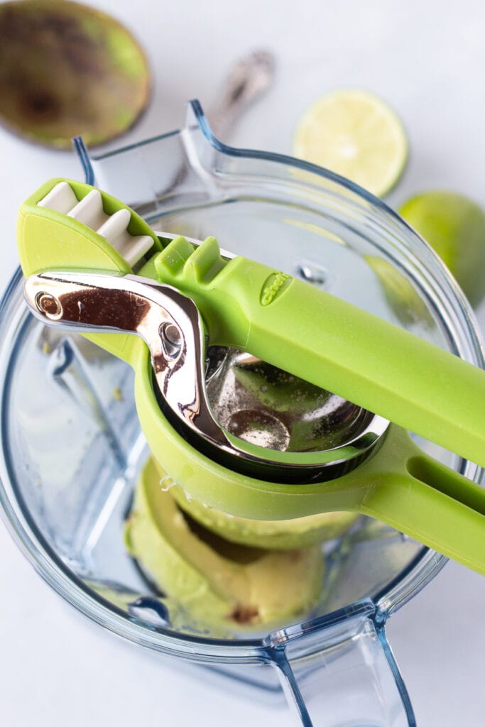 a green handheld juicer juicing a lime into a blender that has avocado in it.
