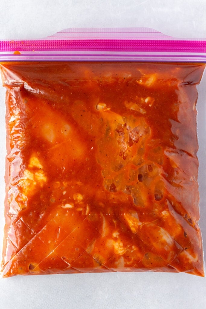 Top down shot of a quart-sized plastic sealable bag with chicken thighs marinating in a red bbq sauce marinade.