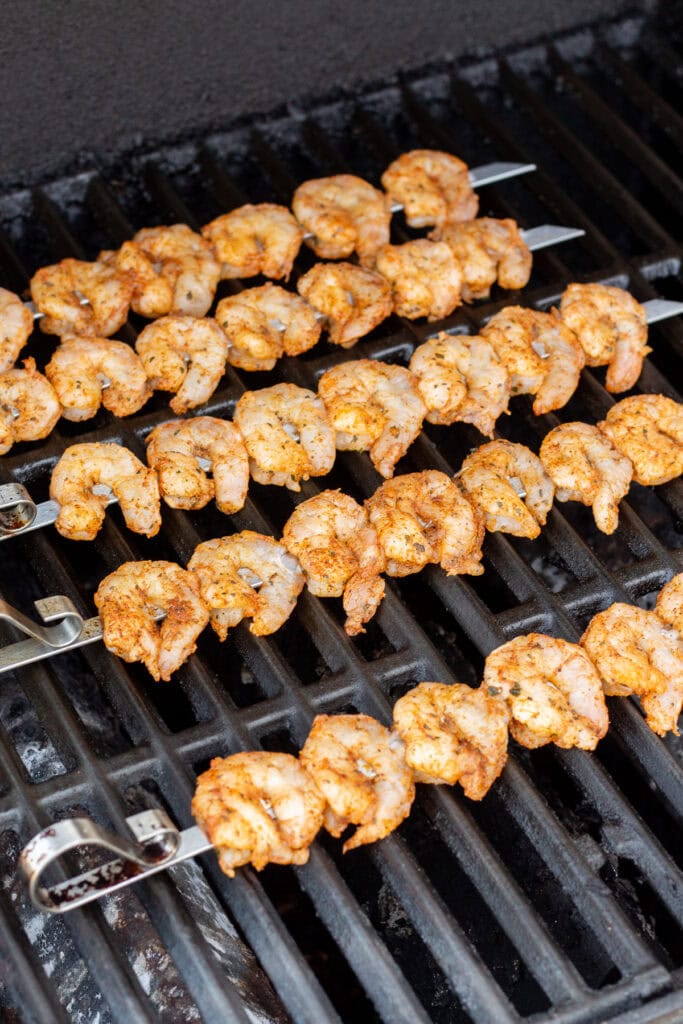 Raw shrimp on metal skewers cooking on a hot grill.