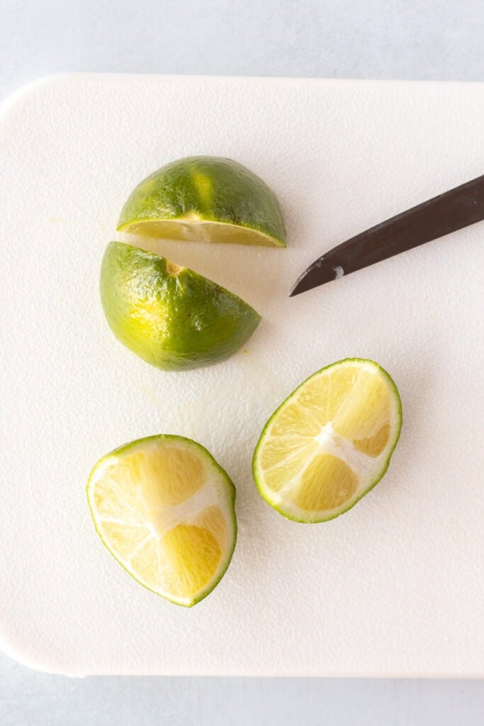 Close up of a lime that's been cut into quarters on a white cutting board next to a sharp knife.