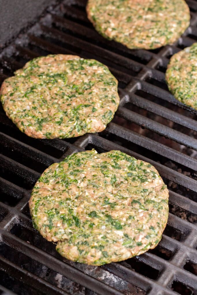Raw meatloaf burger patties with spinach in them on a hot grill.