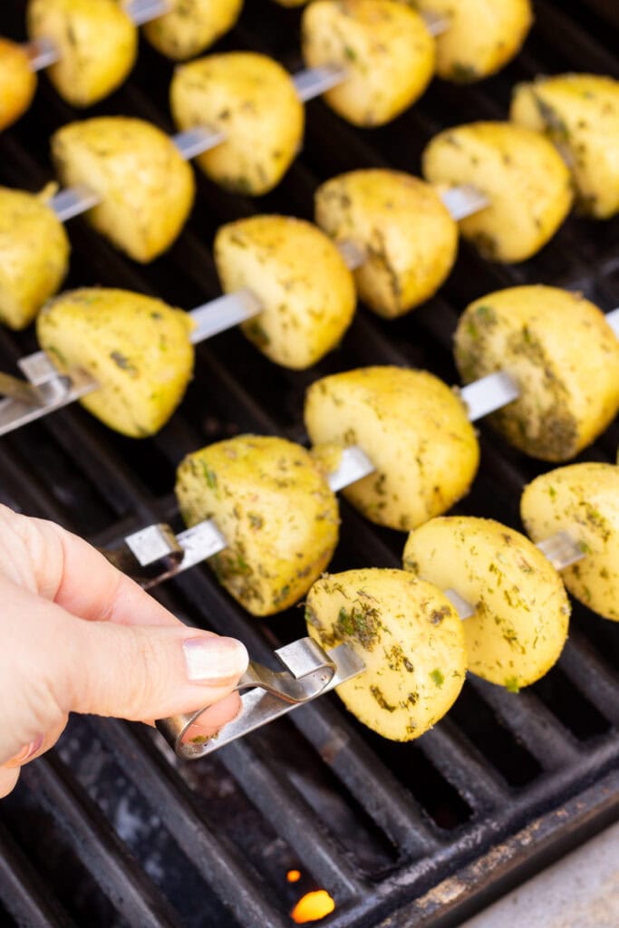 Ranch potatoes on metal skewers being placed on a grill.
