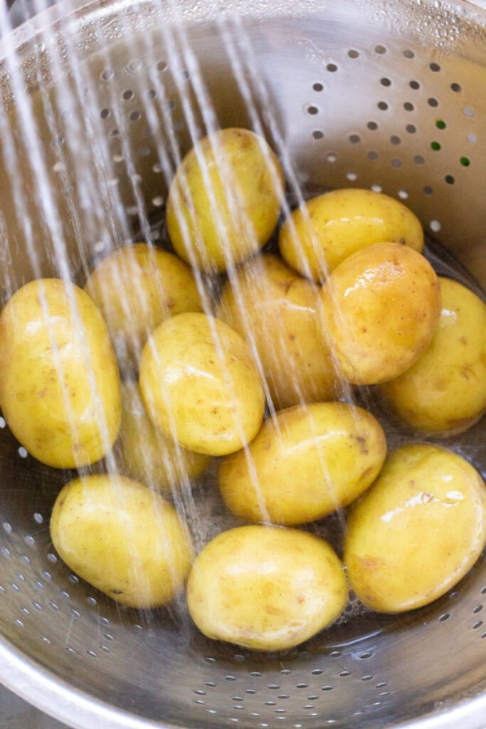 Close up of yellow potatoes in a colander with under water from a kitchen faucet.