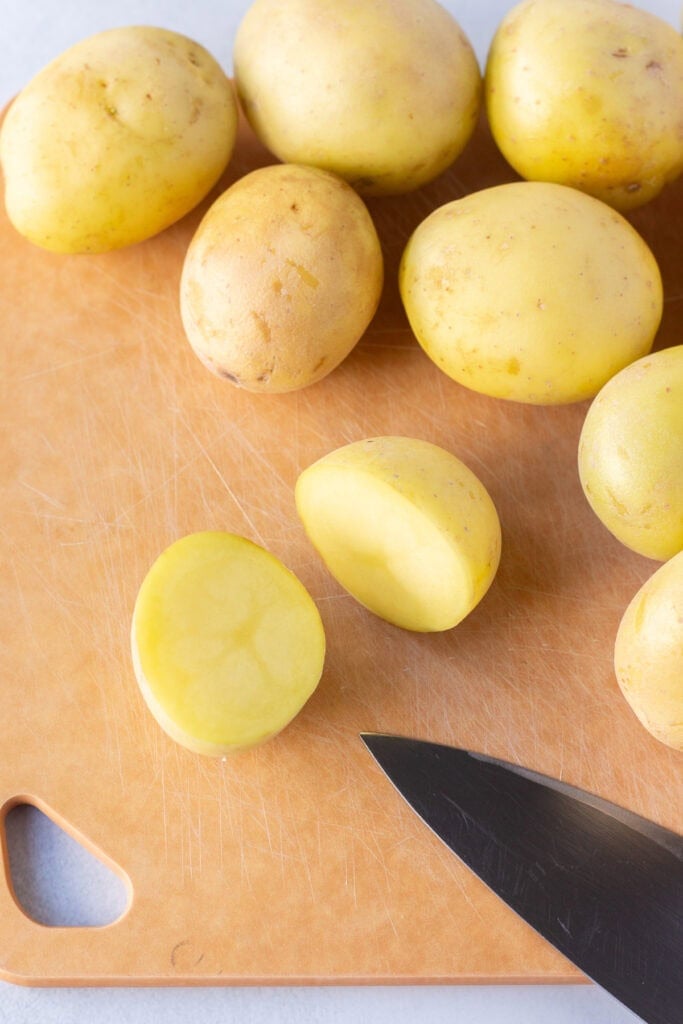 Close up of yellow potatoes on a wood cutting board, with one of them cut in half.