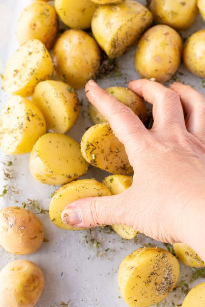 A hand stirring halved yellow potatoes in a glass dish with ranch seasoning and oil on them.